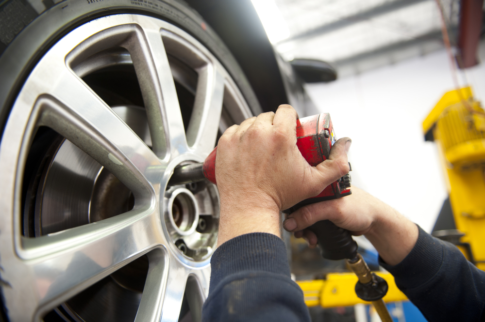 Close Up of hands of mechanic changing wheel of a limousine, with blurred background of garage.
